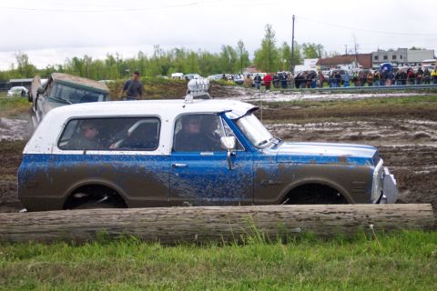 1978 Ford Bronco - A blue and white SUV is stuck in the mud with spectators in the background.