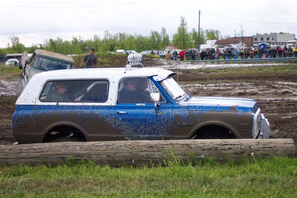 Blue and white SUV stuck in mud, side view. Log in foreground