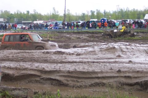 1978 Ford Bronco - An orange SUV navigates a muddy obstacle course during an event.