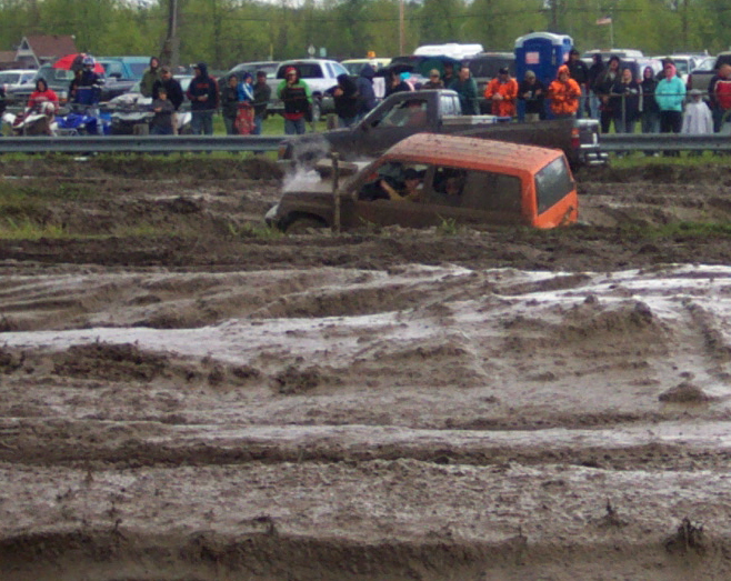 orange SUV stuck deep in mud pit with spectators in background