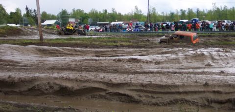 1978 Ford Bronco - Vehicles struggle through a muddy track during an event with onlookers watching.