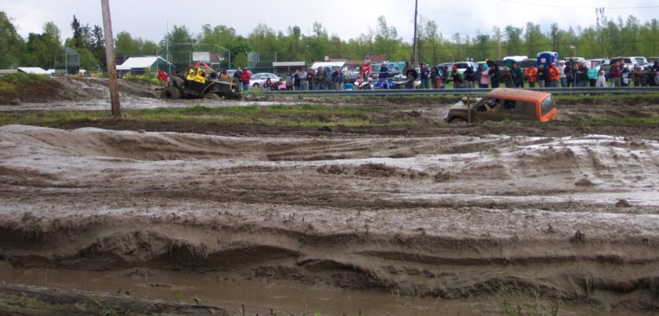 Orange SUV stuck in mud pit with spectators in background