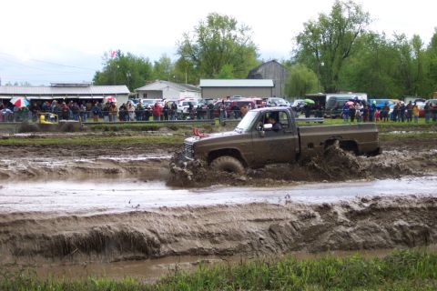 1978 Ford Bronco - Pickup truck navigates a muddy track during an event with onlookers present.