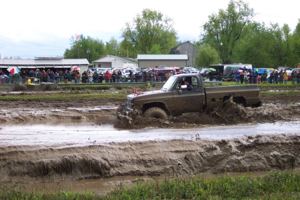 Brown pickup truck stuck in a mud bog with spectators in the background