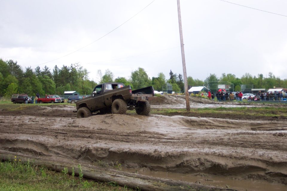 Muddy pickup truck driving through a mud pit with spectators in the background