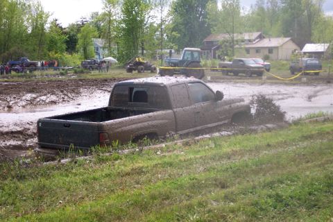 1978 Ford Bronco - A pickup truck is stuck in the mud during an event, with a tractor and other vehicles visible in the background.
