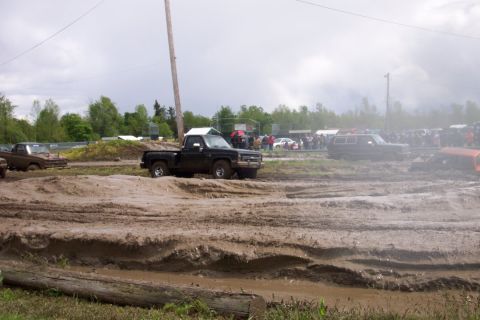 1978 Ford Bronco - Multiple trucks and SUVs navigate a muddy off-road course under an overcast sky.