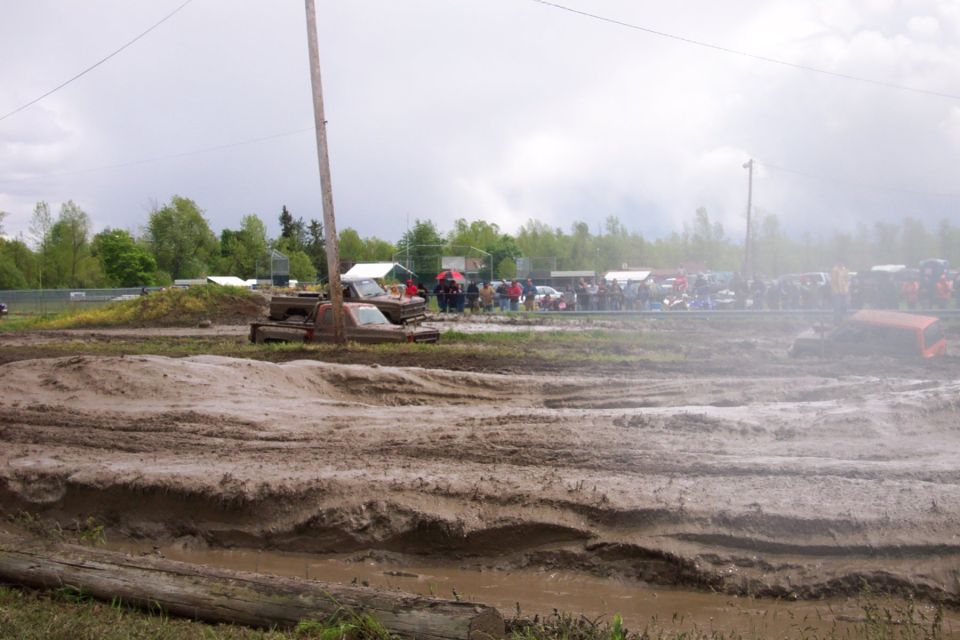 Muddy field with several vehicles and a crowd of spectators watching an event