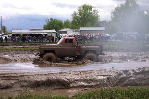 1978 Ford Bronco - A heavily muddied pickup truck navigates a challenging mud bog with onlookers gathered.