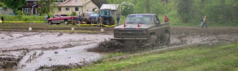 1978 Ford Bronco - Pickup truck navigates a muddy track during an event, with other vehicles and spectators present.
