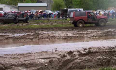 1978 Ford Bronco - Two off-road vehicles navigate a challenging muddy course, with spectators watching in the background.