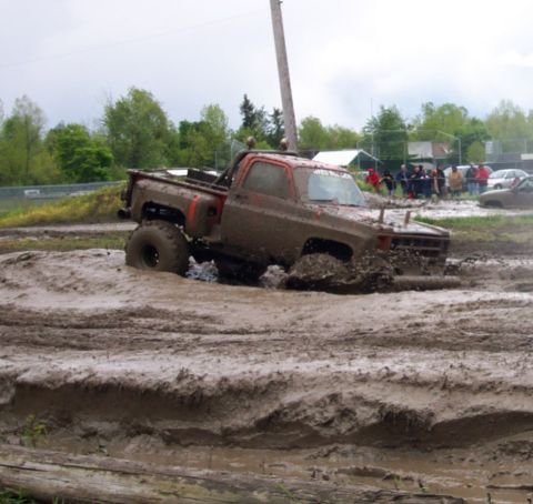 1978 Ford Bronco - A muddy pickup truck is stuck in a mud pit during an event, with spectators in the background.