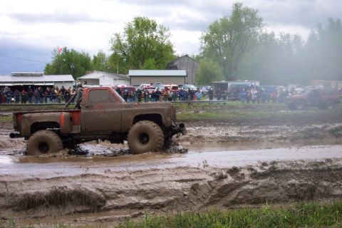 1978 Ford Bronco - A heavily mud-covered pickup truck participates in a mud bog event, with a crowd watching from the sidelines.