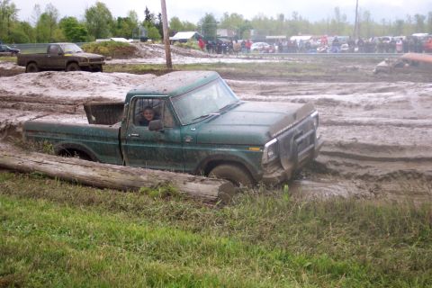 1978 Ford Bronco - A green pickup truck is stuck in deep mud, with a crowd watching in the background.