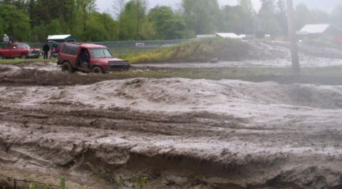 1978 Ford Bronco - A red SUV is stuck in a muddy off-road course with other vehicles in the background.