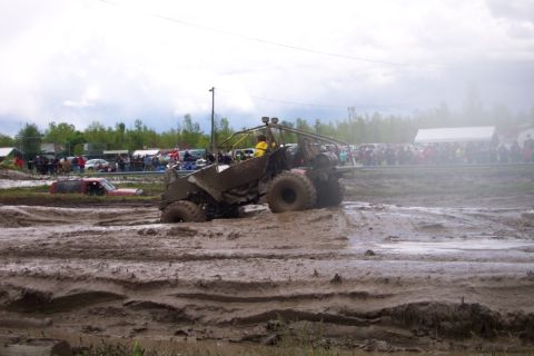 1978 Ford Bronco - An off-road vehicle navigates a challenging mud pit, with a crowd of spectators watching the event.