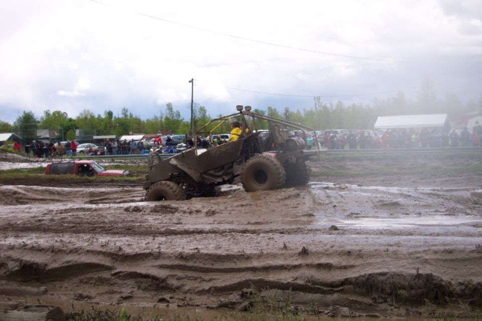 Off-road vehicle stuck in mud pit with spectators in background