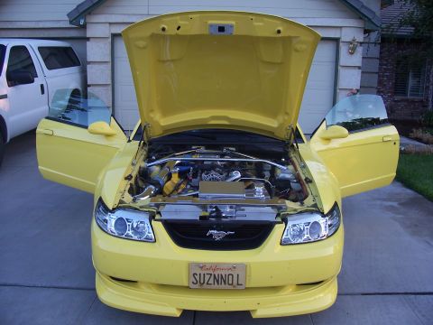 2002 Ford Mustang - Front view of a yellow 2002 Ford Mustang with its hood and doors open, revealing the engine.