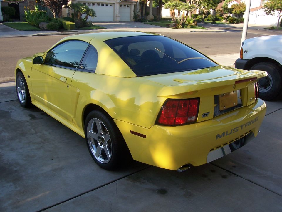 Yellow 2002 Ford Mustang GT coupe parked on driveway, rear 3/4 view