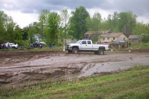 1978 Ford Bronco - A white pickup truck is seen in a muddy outdoor area with several houses and trees in the background.