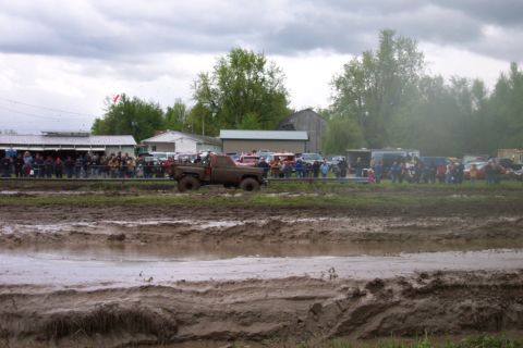 1978 Ford Bronco - A muddy pickup truck navigates a challenging mud bog while onlookers observe the event.