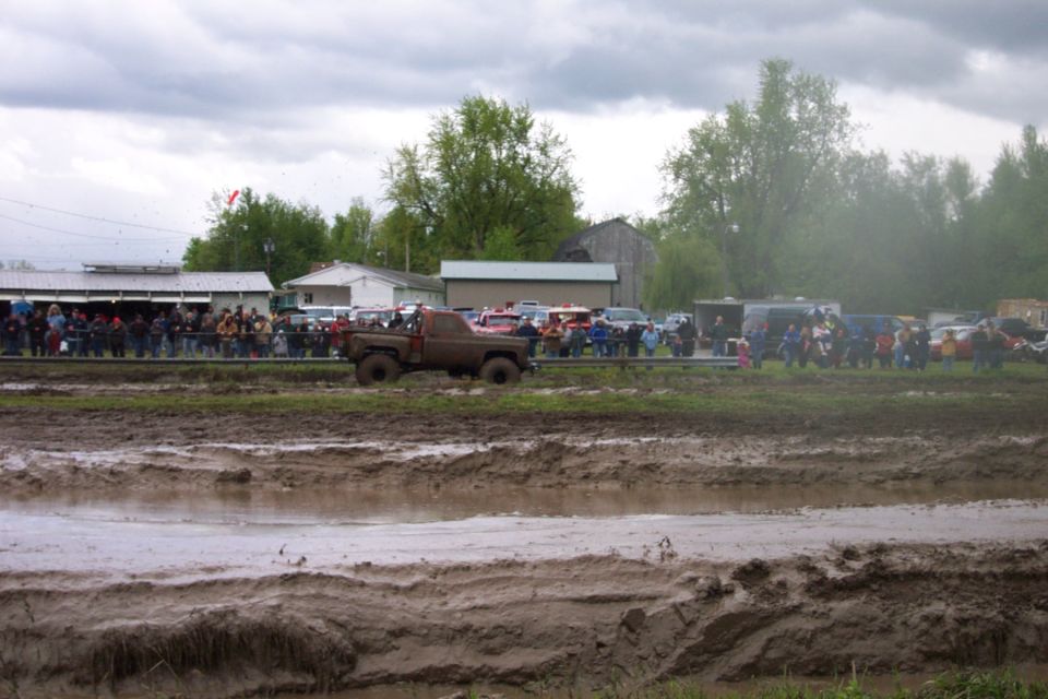 Brown pickup truck driving through mud, spectators watch from a distance