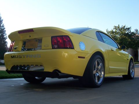 2002 Ford Mustang - A yellow 2002 Ford Mustang GT is viewed from the rear quarter angle, highlighting its distinctive spoiler and badging.