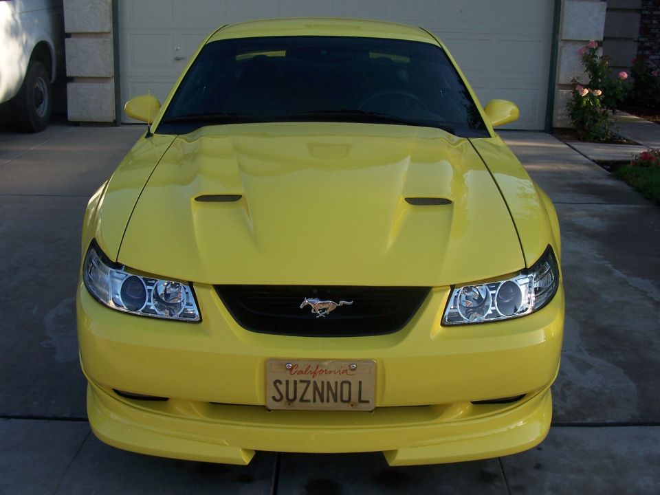 Yellow 2002 Ford Mustang with California plates parked in front of a garage