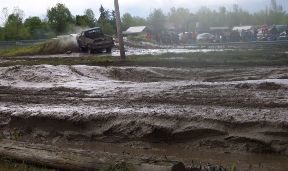 Truck driving through mud pit with spectators in background