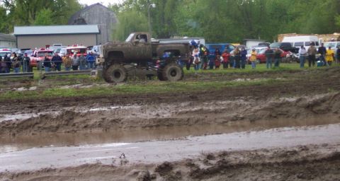 1978 Ford Bronco - A lifted truck navigates a muddy track during an event, with onlookers gathered in the background.