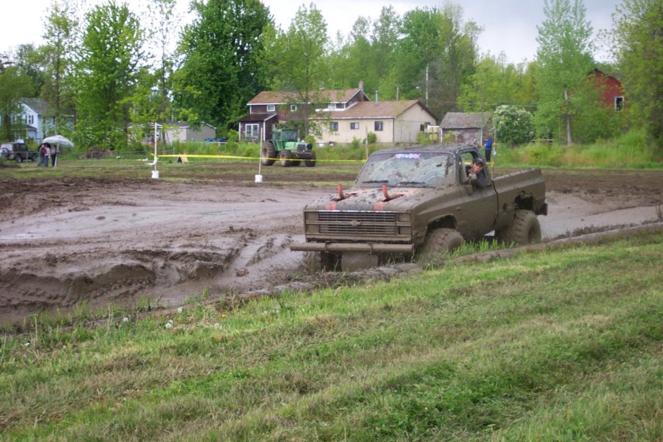 Mud-splattered pickup truck with a lifted suspension navigates a muddy track, its front grille visible