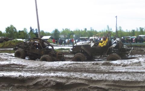 1978 Ford Bronco - Two custom off-road vehicles are stuck deep in the mud during an event, with spectators in the background.