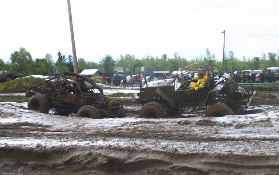 Two off-road vehicles submerged in mud, one with a driver in a yellow suit