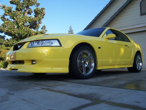 2002 Ford Mustang - A bright yellow 2002 Ford Mustang is parked in front of a house and garage.