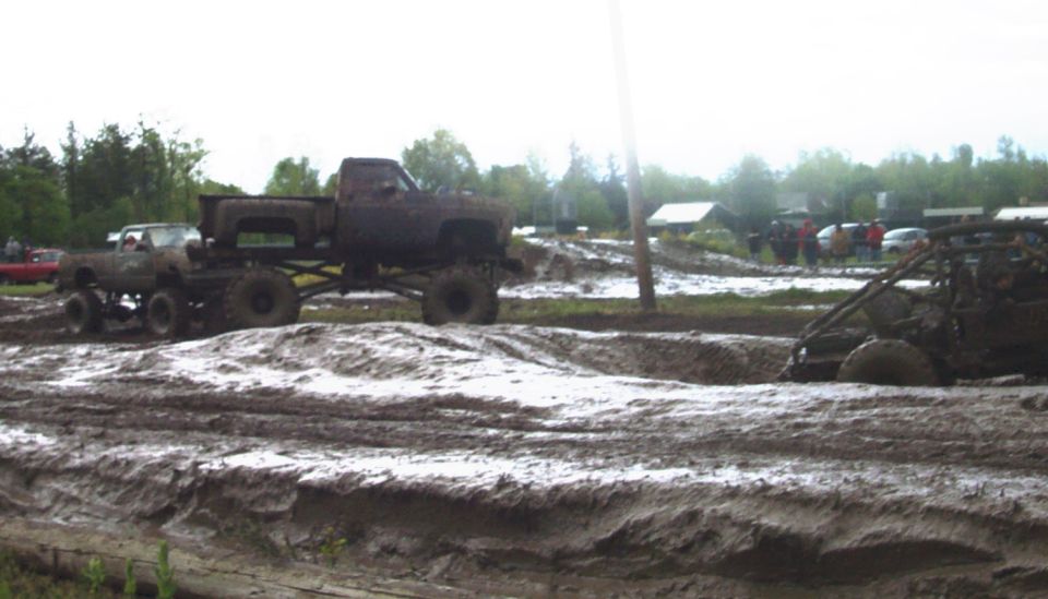Mud bogging scene with lifted trucks and a buggy stuck in the mud