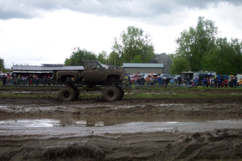 Muddy lifted pickup truck driving through a mud pit with spectators in the background
