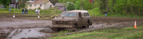 1978 Ford Bronco - This SUV is navigating a challenging mud course, kicking up a lot of spray.