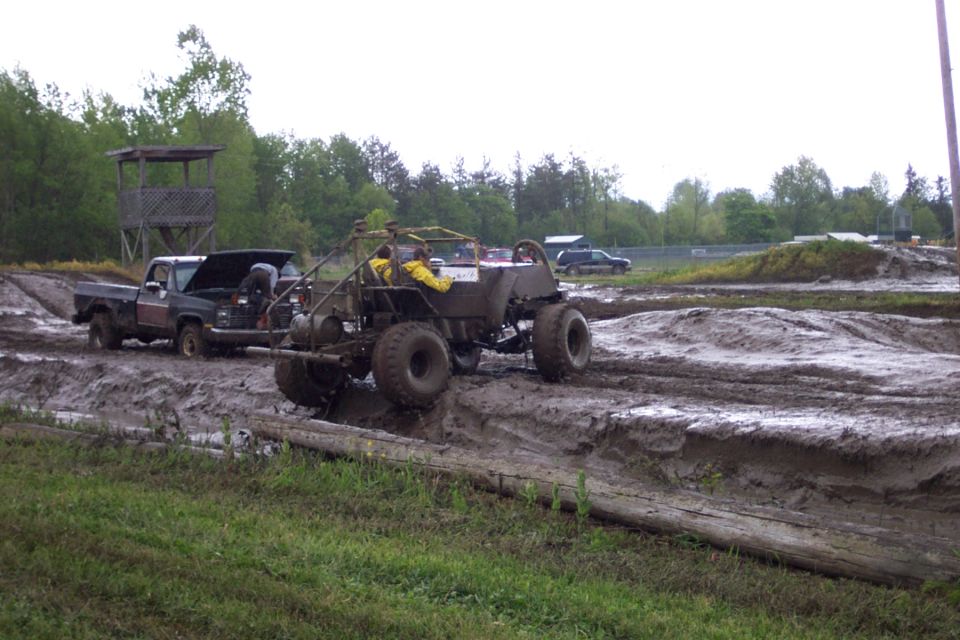 Mud bog with a buggy stuck in the mud and a pickup truck with its hood open