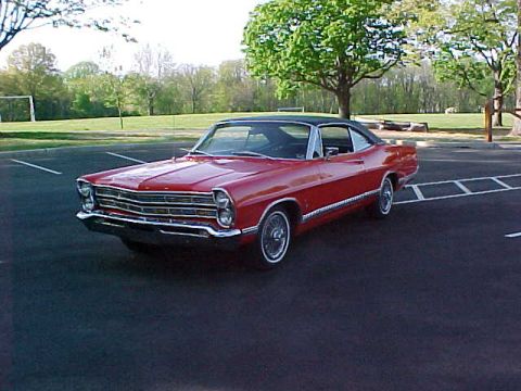 1967 Ford Galaxie - A red 1967 Ford Galaxie coupe is parked in an outdoor lot with trees and a soccer goal in the background.