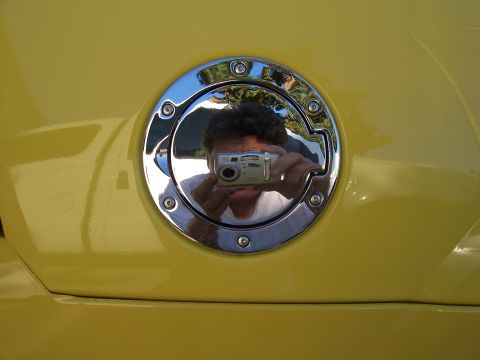 2002 Ford Mustang - Chrome fuel filler door on a yellow vehicle shows a reflection of the photographer and their camera.