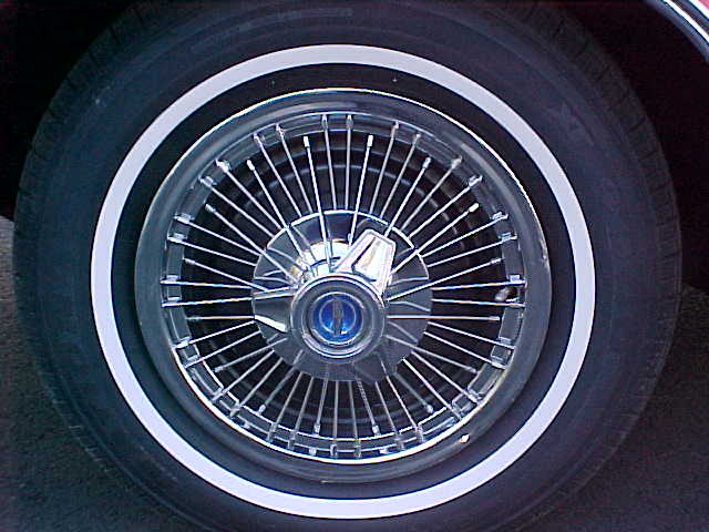 Chrome wire-spoke wheel with whitewall tire and blue center cap emblem