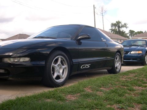 1997 Ford Probe - A black 1997 Ford Probe GTS is parked in front of a blue Ford Mustang on a cloudy day.