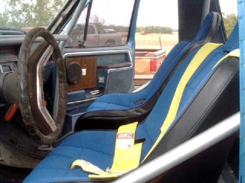 1984 Ford Bronco - The interior of a vehicle features racing seats and a roll cage, with another truck visible through the window.