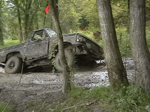 1988 Ford Bronco - A heavily muddied truck is stuck off-road, with trees surrounding it.