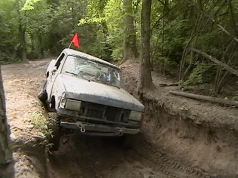 1988 Ford Bronco - A pickup truck navigates a challenging, muddy off-road path through a wooded area.