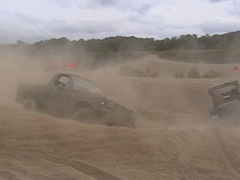 1988 Ford Bronco - Two vehicles are seen off-roading, kicking up a lot of dust on a cloudy day.