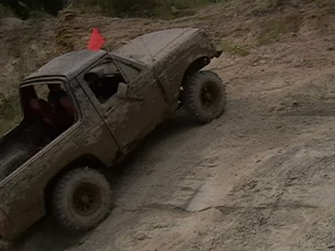 1988 Ford Bronco - A muddy truck navigates a dirt incline, its red flag a stark contrast against the brown terrain.