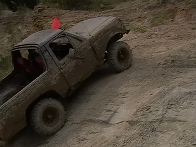 Mud-covered truck with red flag on roof, driving on dirt hill