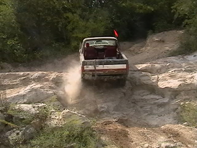 Pickup truck driving up a dusty, rocky incline with trees in the background