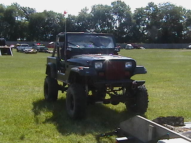 Lifted Jeep Wrangler with red-trimmed grille on big tires parked on grass at an outdoor event